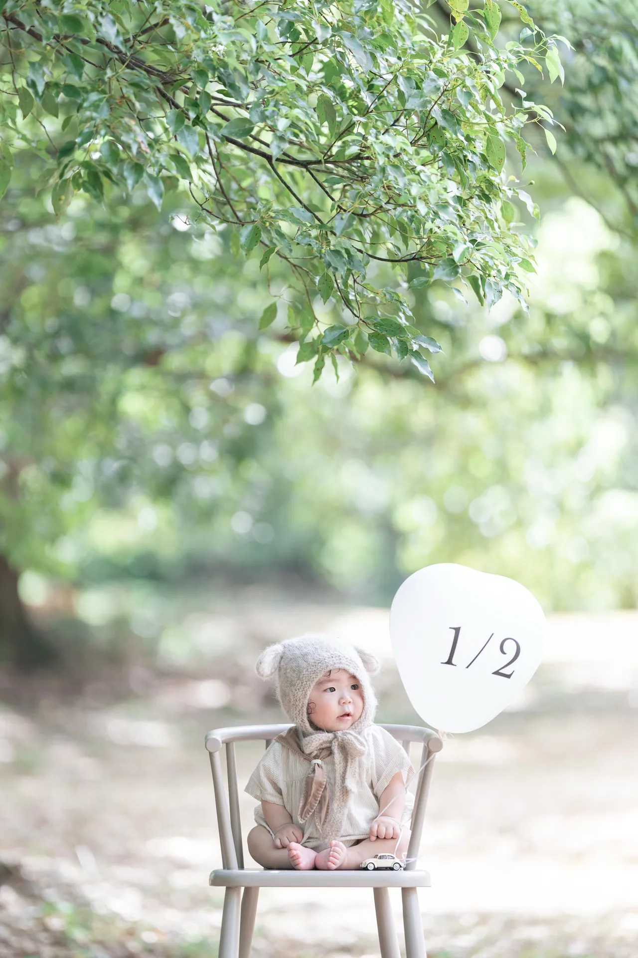 木陰の椅子に座る赤ちゃんと「1/2」の飾りの写真