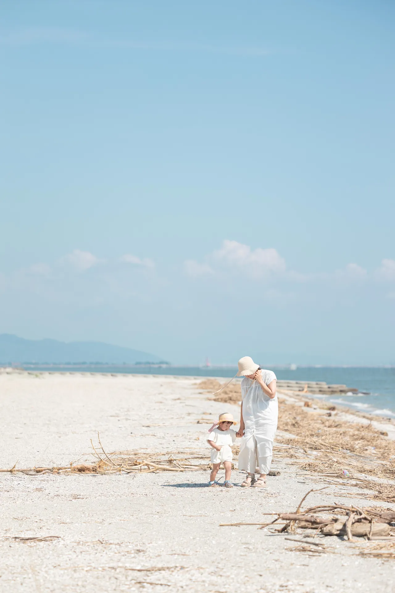白い砂浜を、母親と子どもが歩いている写真