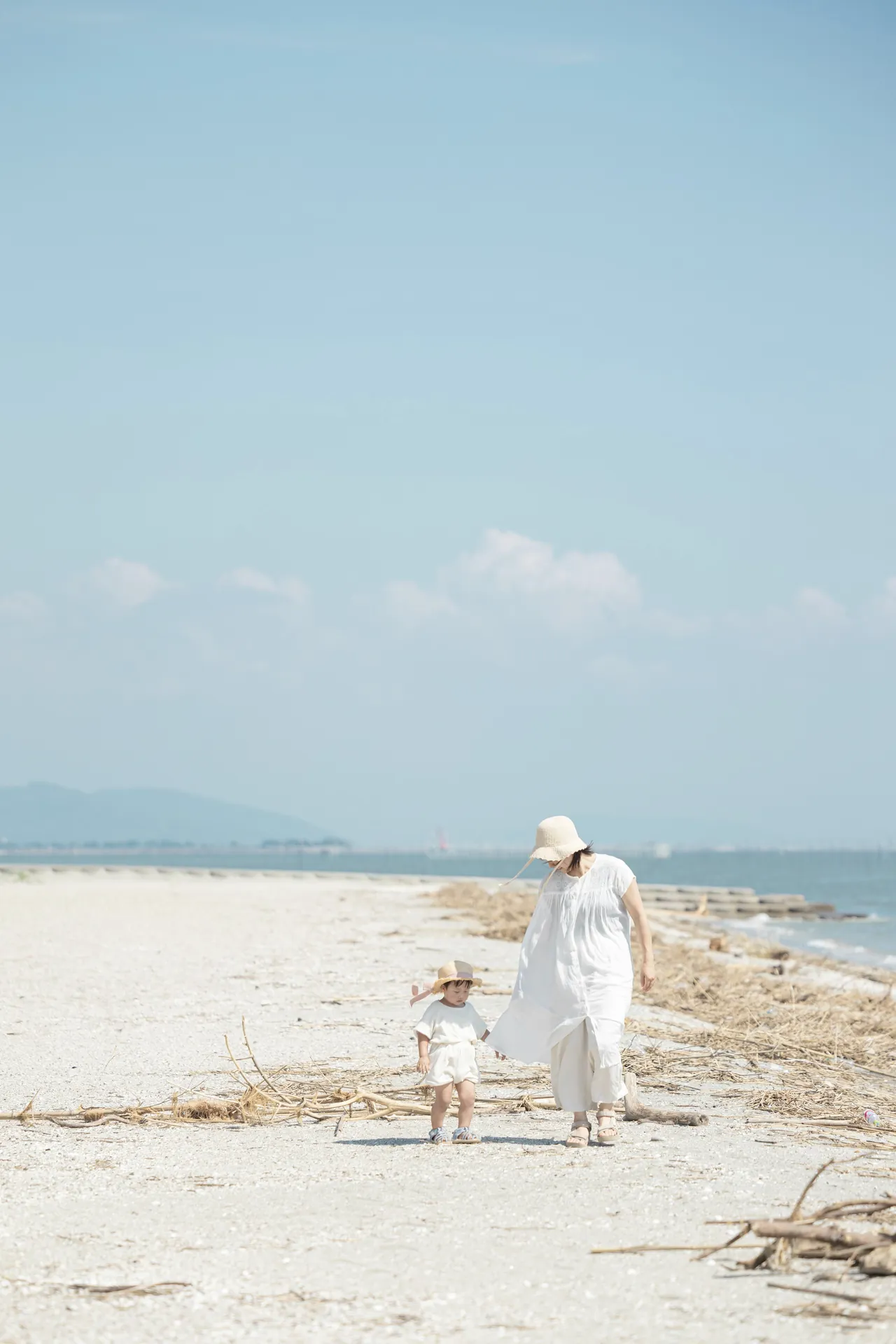 白い砂浜で、母親と子どもが歩いている写真