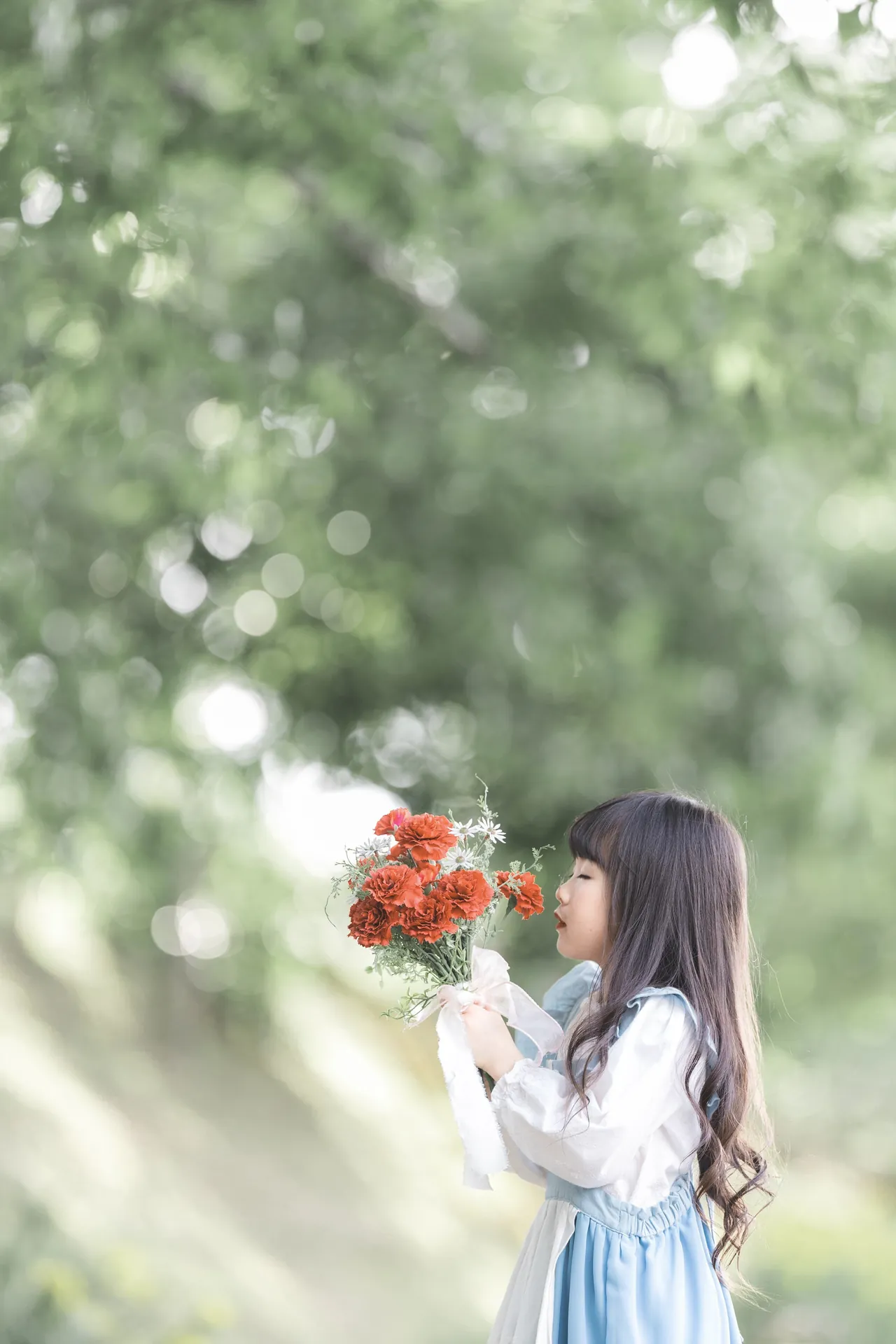 赤い花束の香りをかぐ、女の子の横顔の写真