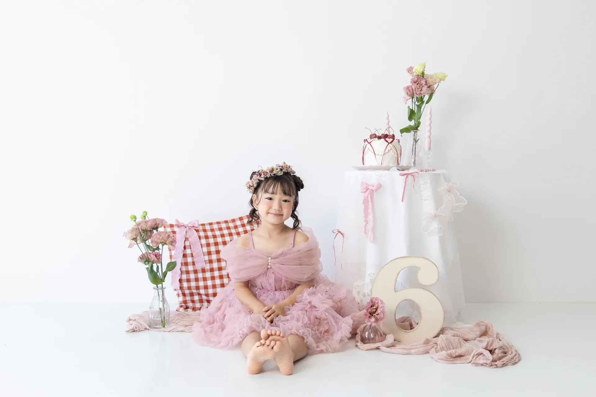 白い背景のセットで、ピンクのドレスの女の子と「6」の飾りの写真