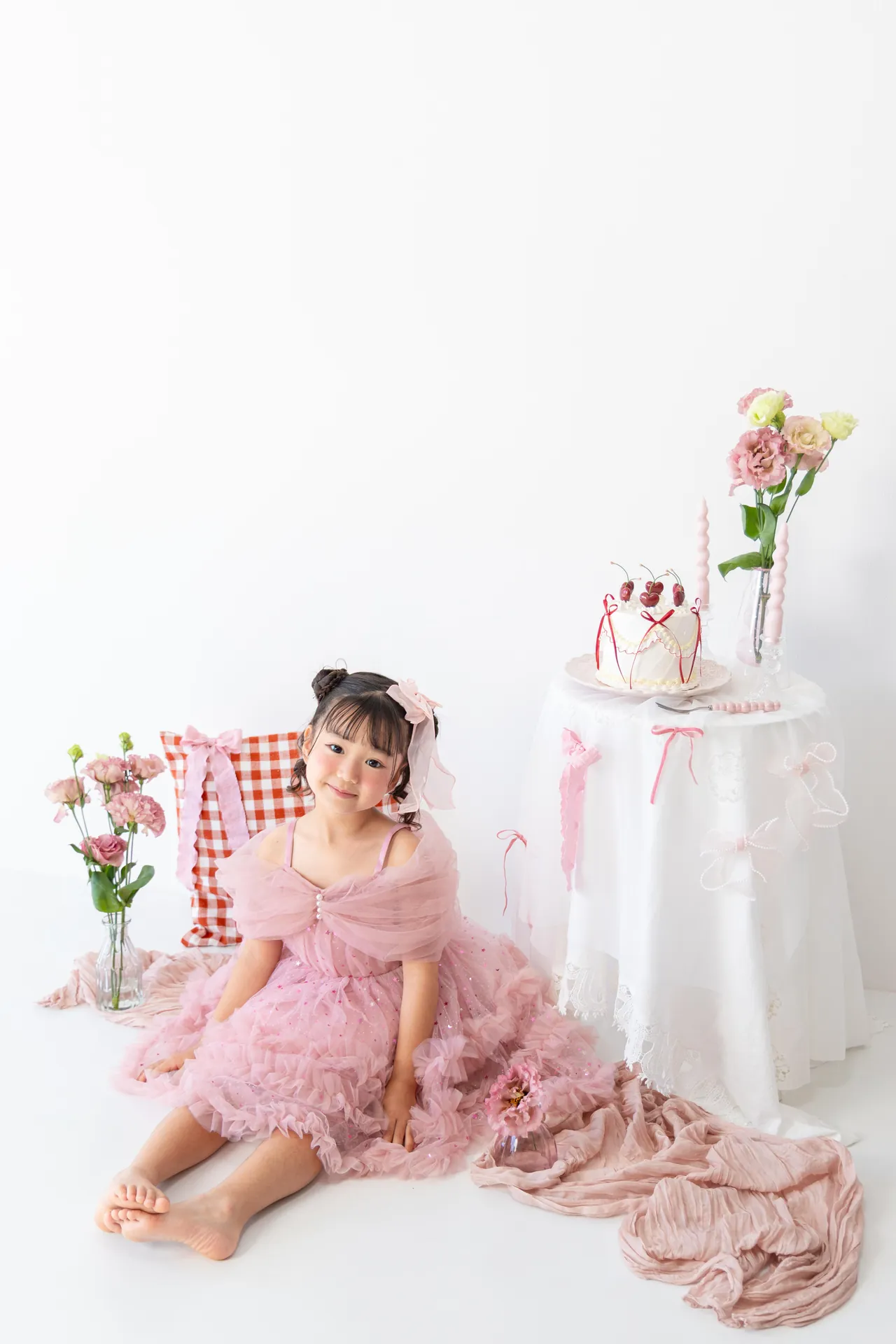 ケーキのテーブルのそばで、ピンクのドレスの女の子が座っている写真