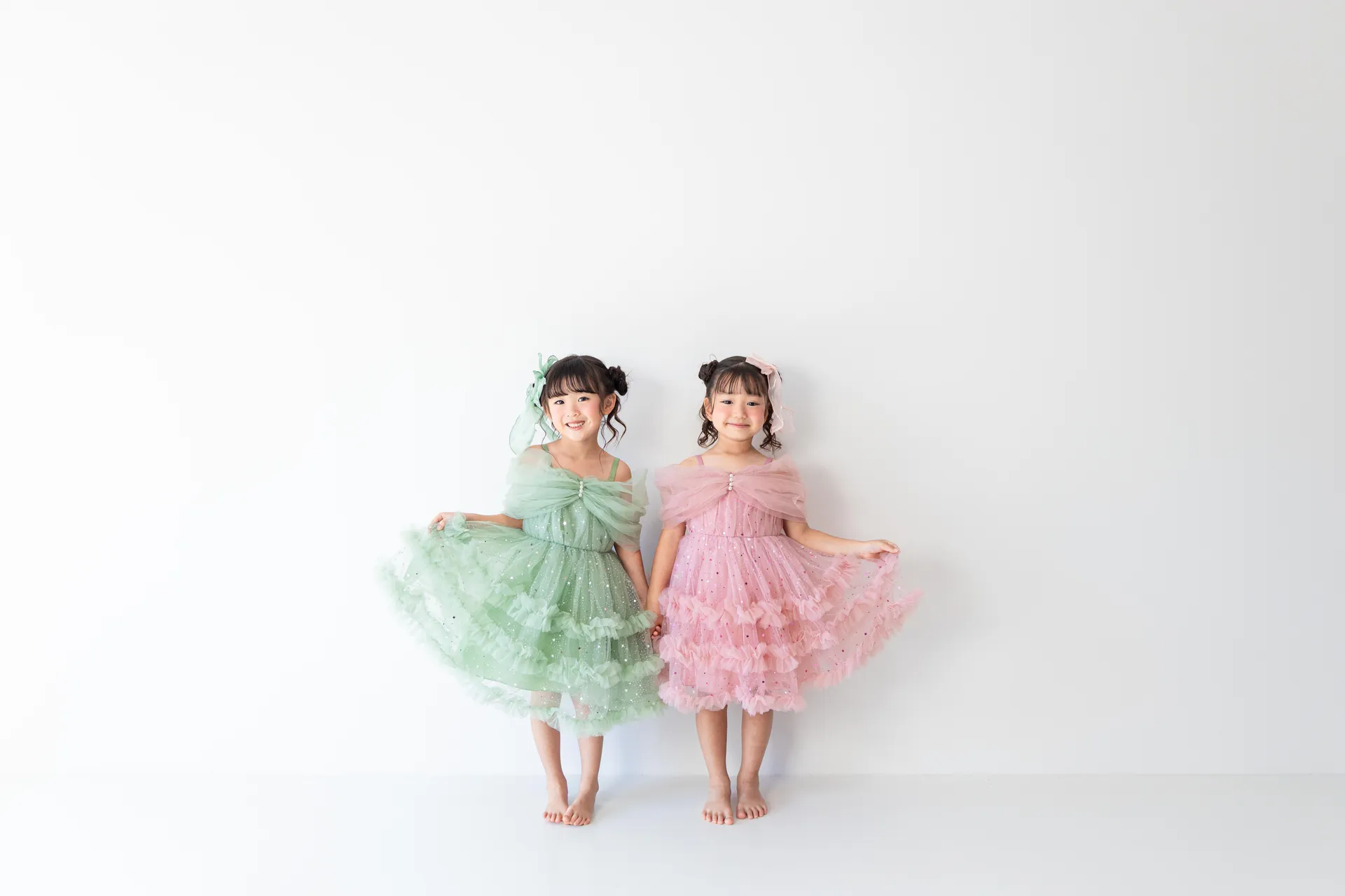 白い背景の前で、グリーンとピンクのドレスの二人が並んでいる写真