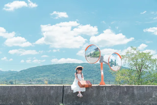 青空とカーブミラーの前で、堤防に座る女の子の写真